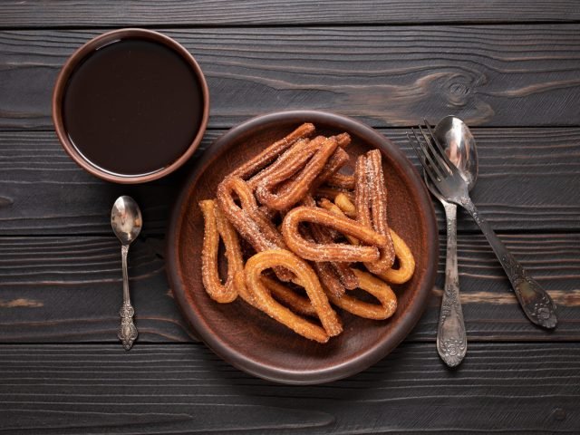 Homemade churros with chocolate on a dark wooden rustic background.